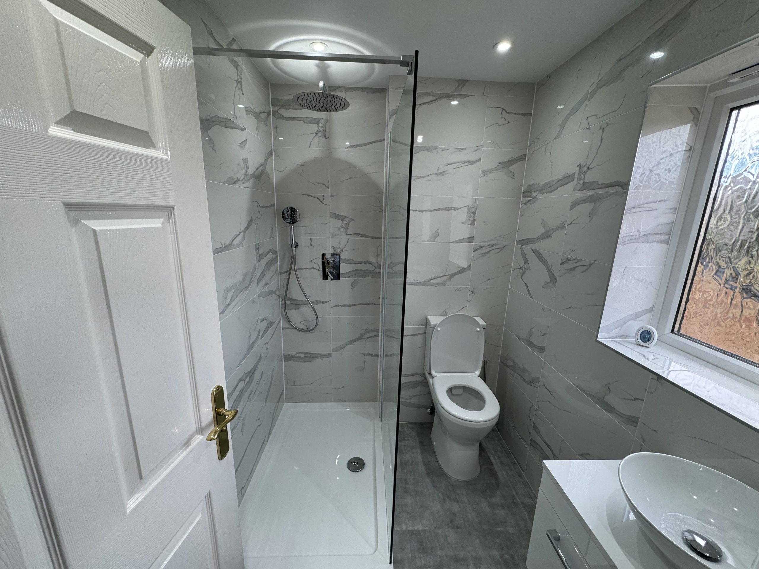 Modern bathroom with grey marble-tiled walls, a walk-in glass shower, ceiling rain shower head, and a white sink with bowl basin—perfect inspiration for your next kitchen and bathroom showroom design or installation project.