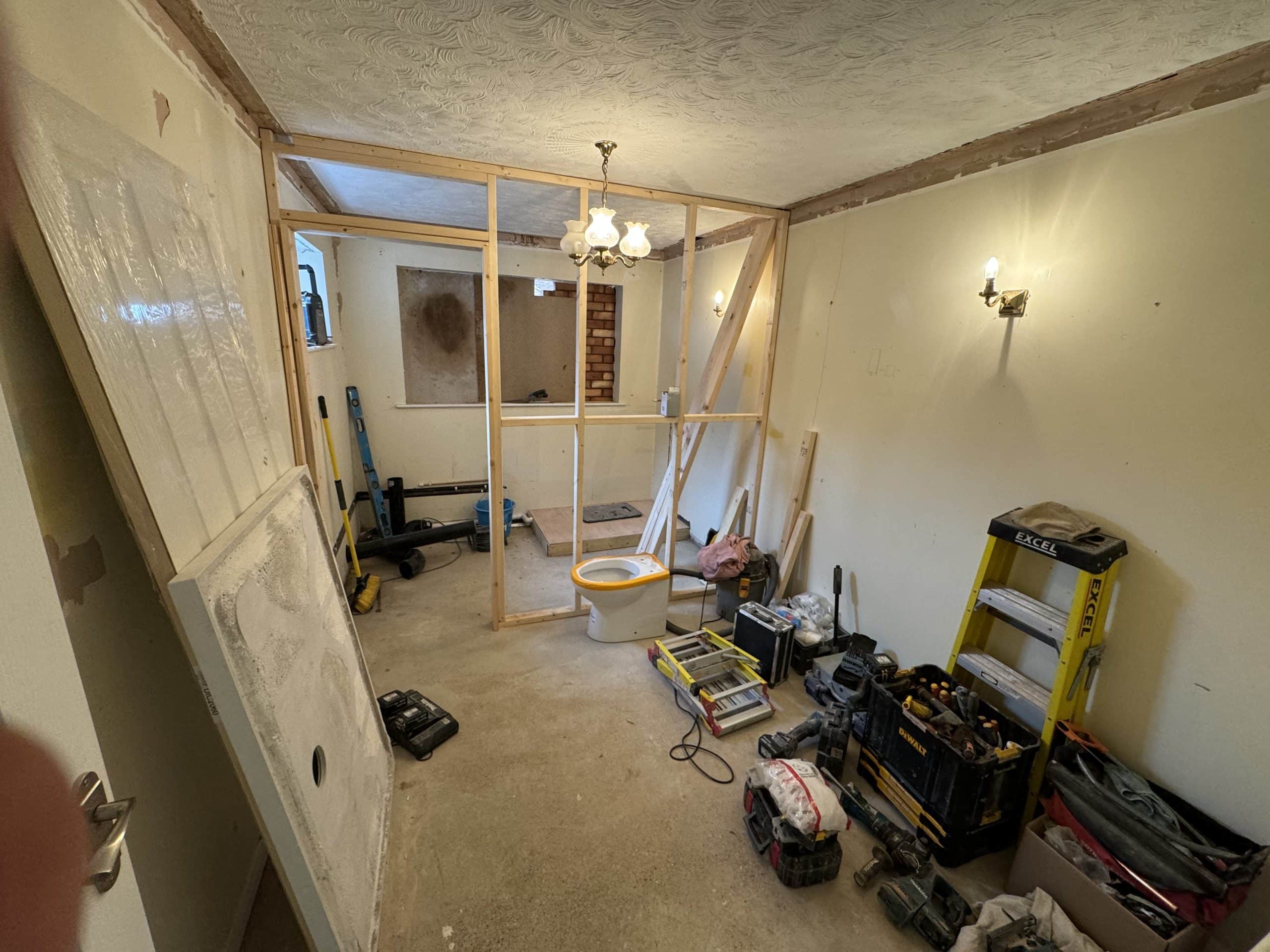 A room undergoing refurbishment with tools and equipment on the floor, a wooden framework being built, exposed walls, and various light fittings—ideal for kitchen and bathroom showroom installation or design projects.