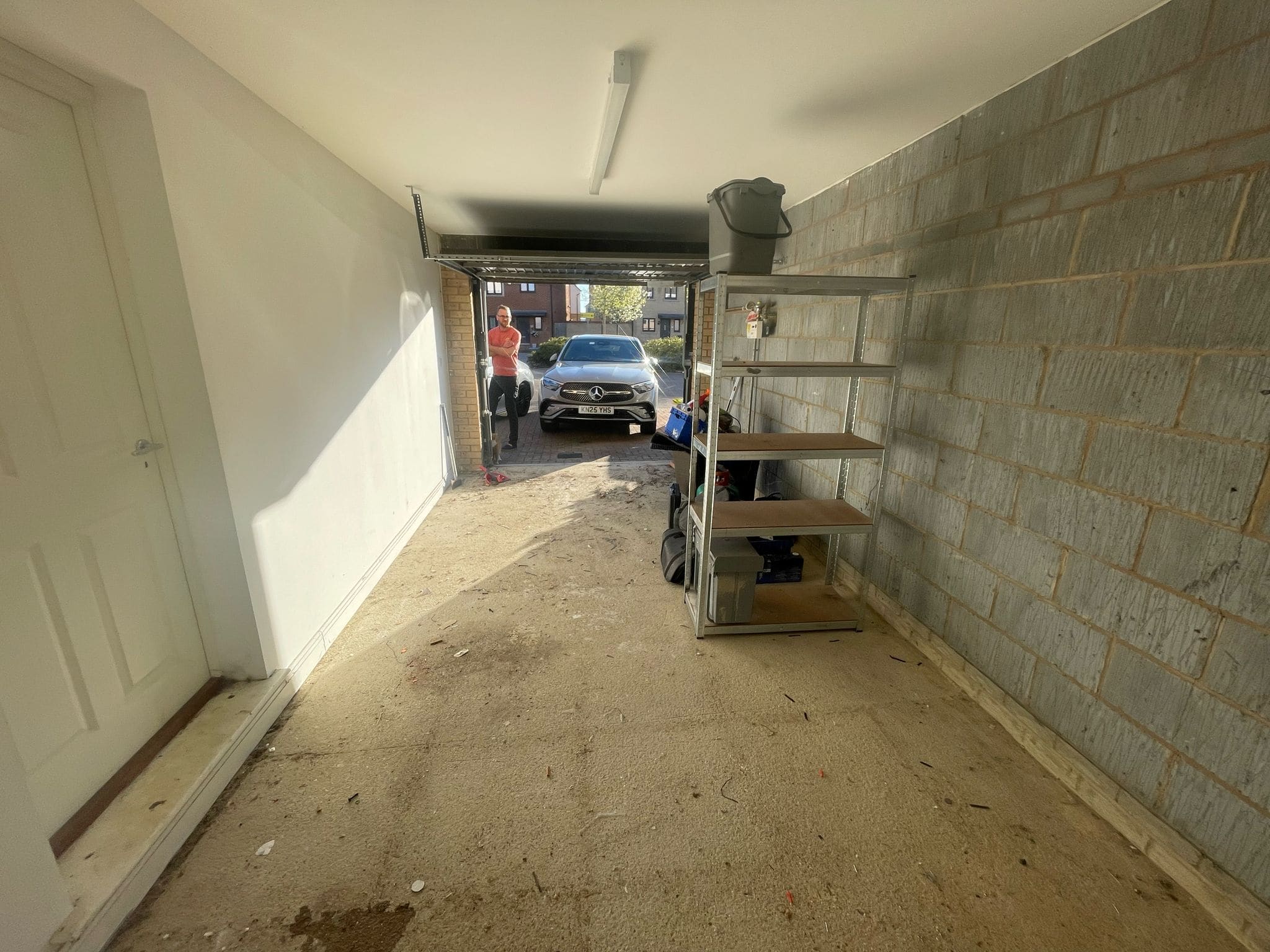 View from inside a mostly empty garage with unfinished walls, a metal shelving unit on the right, and an open door leading outside where a car is parked—ideal for kitchen and bathroom showroom installation supply design storage.