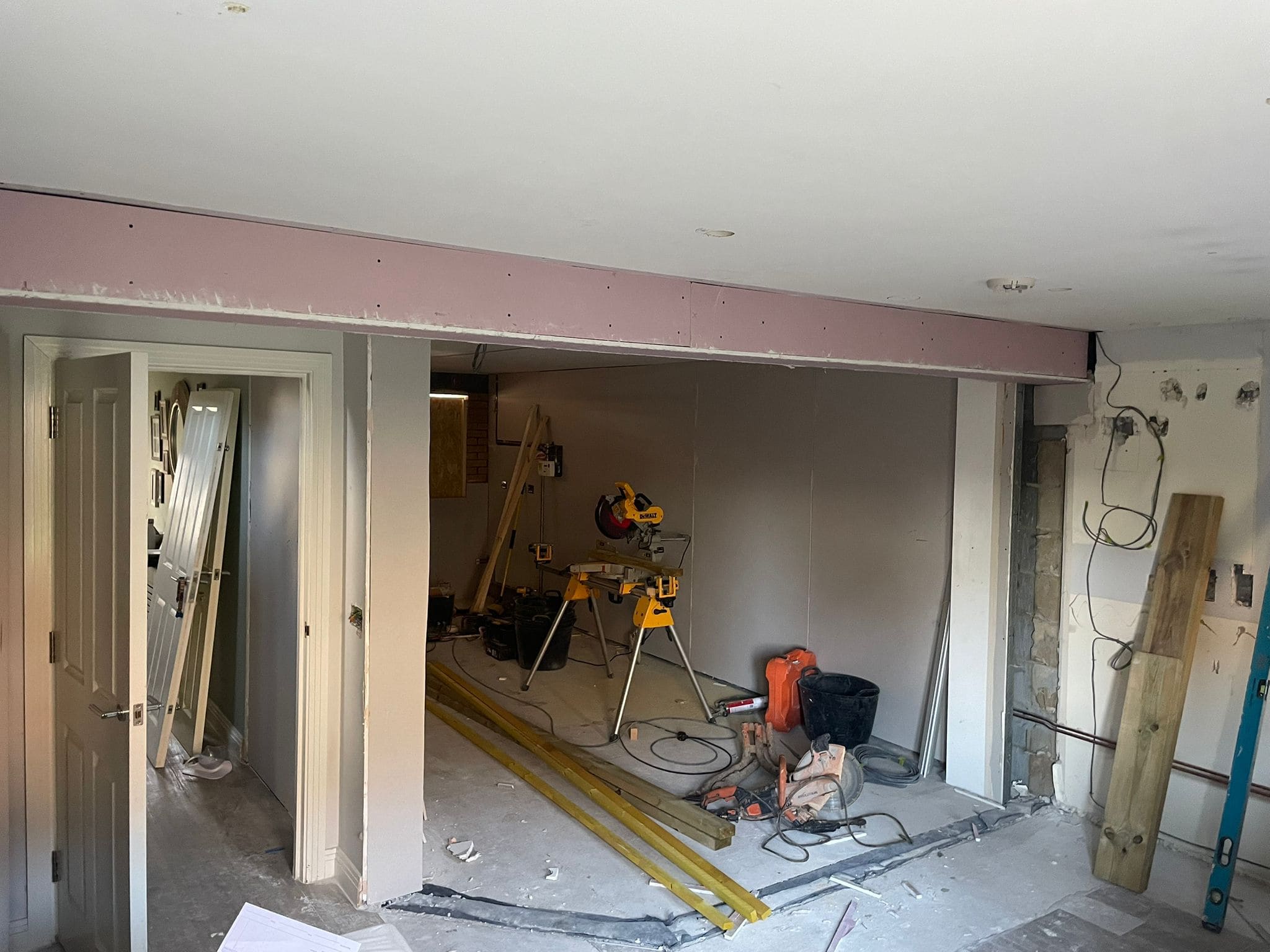 A room under renovation with construction tools and building materials hints at an upcoming kitchen and bathroom showroom installation. The dusty, unfinished floor, exposed wires, and new plasterboard showcase the early stages of supply and design work.