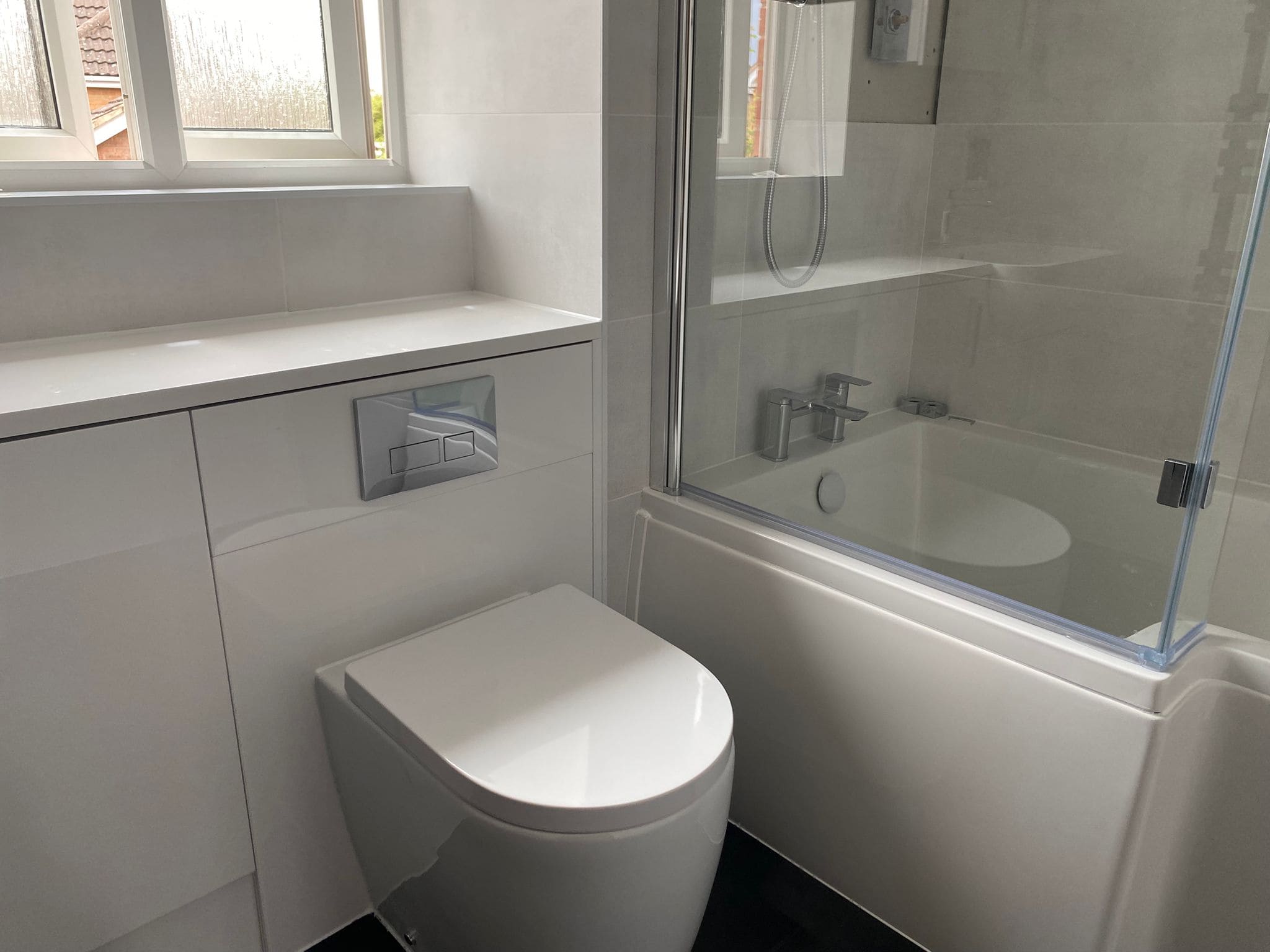 A modern bathroom with a white toilet, built-in cupboard, glass-enclosed bath, shower fittings, and a frosted window letting in natural light—perfect inspiration for any kitchen and bathroom showroom or installation design.